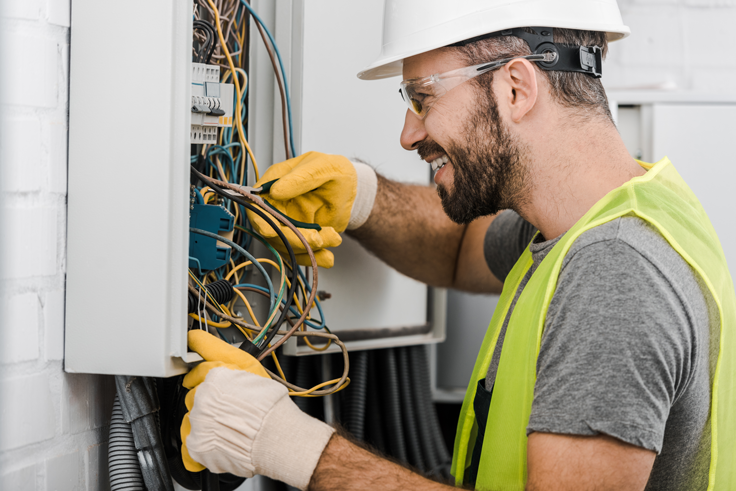 side-view-of-smiling-handsome-electrician-repairing-electrical-box-with-pliers-in-corridor